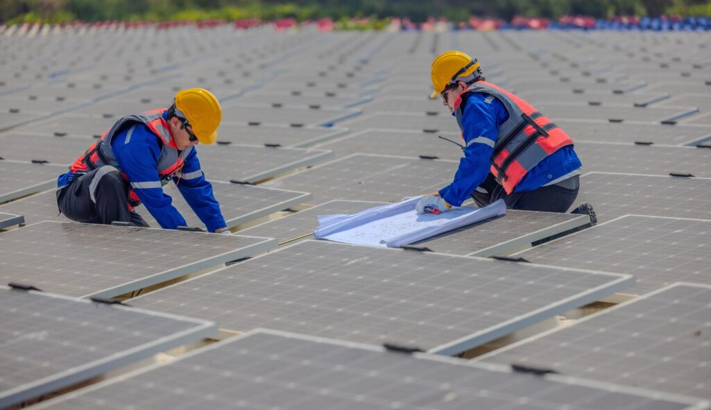 Two workers wearing protective gear installing solar panels with many already installed in the background